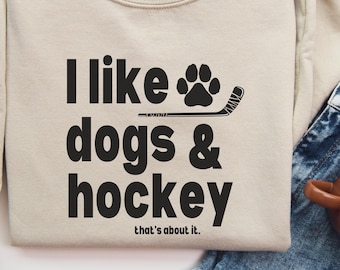 May include: A beige sweatshirt with the text "I like dogs & hockey that's about it." in black. A paw print and hockey stick are above the text.