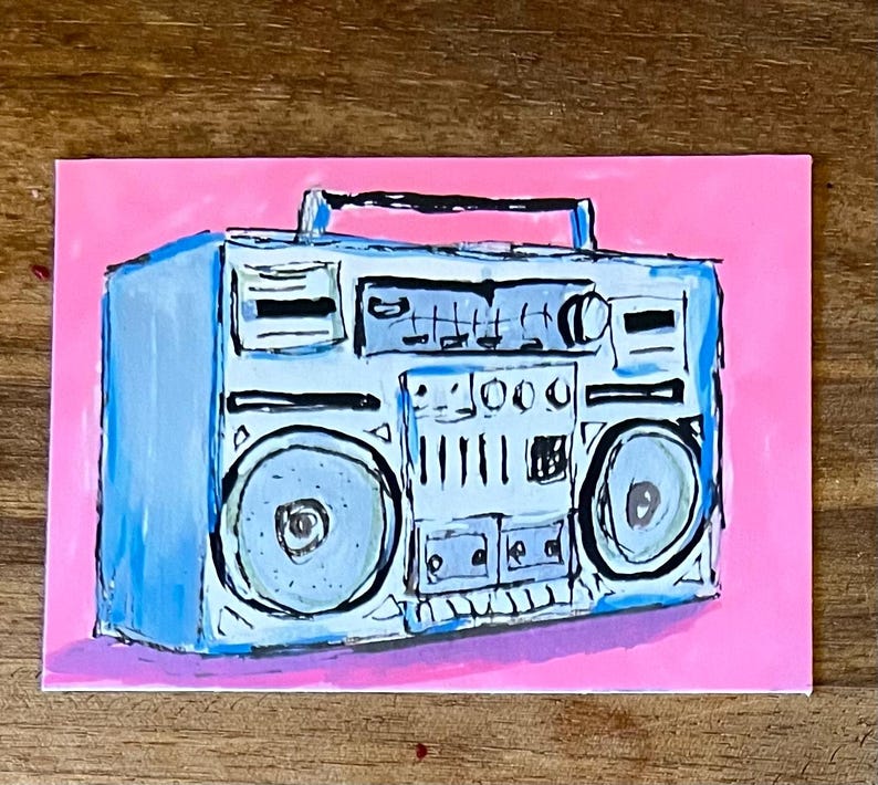 May include: A hand-painted illustration of a light blue boombox on a bright pink background. The boombox features a top handle, two large circular speakers, a central control panel with knobs and buttons, and a cassette deck area with black outlines.