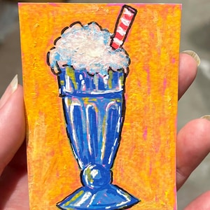 May include: A small rectangular painting featuring a blue milkshake in a tall glass with a white whipped cream topping and a red and white striped straw, set against a vibrant orange and yellow textured background with visible brushstrokes.