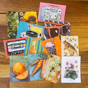 May include: A collection of rectangular art prints featuring diverse illustrations including a boombox, sunglasses, a cassette tape labeled Side Road Mix 90, a record player, a cat, bees on a honeycomb, an orange, carrots, flowers, and a moth.