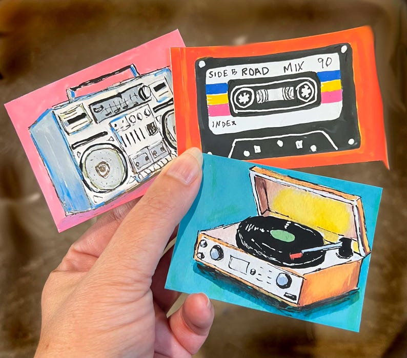 May include: Three rectangular stickers featuring hand-drawn illustrations of vintage audio equipment. One sticker shows a blue boombox on a pink background, another a black cassette tape labeled SIDE B ROAD MIX 90, and the third a record player.