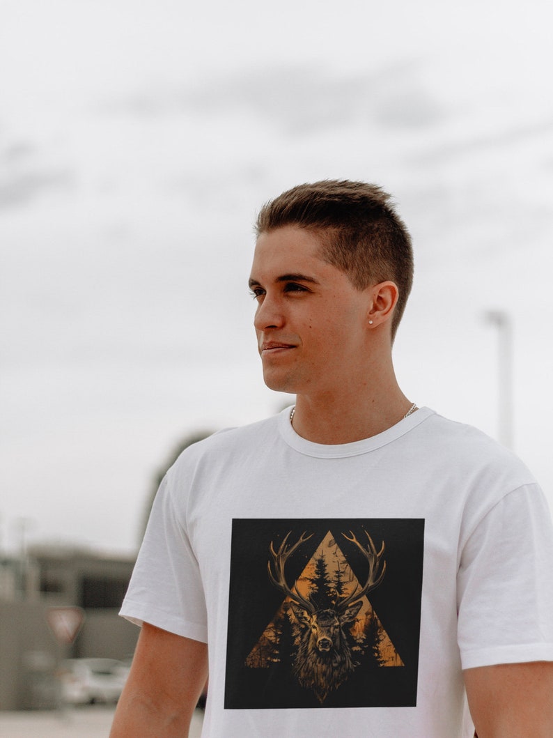 May include: A white t-shirt with a graphic print of a deer's head in a triangle shape with trees and a sunset behind it.