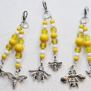 Puede incluir: Tres llaveros de cuentas amarillas y blancas con abalorios de abeja plateados. Cada llavero tiene un clip plateado.