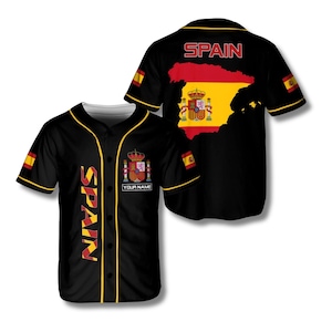 May include: Black baseball jersey with yellow trim and the word "SPAIN" in yellow. The jersey features the Spanish coat of arms and flag. The back of the jersey displays the word "SPAIN" and a map of Spain in the colors of the flag.