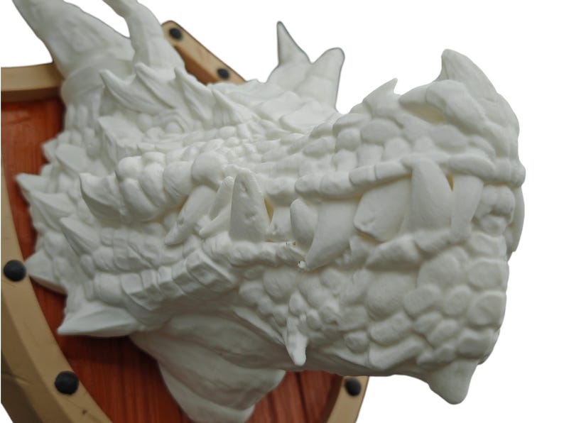 Puede incluir: Escultura de cabeza de drag&oacute;n blanco montada en una placa de madera. La boca del drag&oacute;n est&aacute; abierta, revelando dientes afilados. La escultura est&aacute; detallada con escamas y piel texturizada.