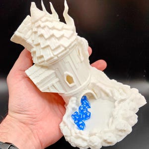 May include: White 3D printed tower with a crumbling roof and a hole in the side. The tower is sitting on a base that looks like a cloud. There are blue dice with white numbers inside the tower.