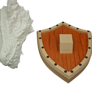 Puede incluir: Una escultura de cabeza de drag&oacute;n blanca con una superficie texturizada detallada. La escultura est&aacute; montada en un escudo de madera con un patr&oacute;n de veta de madera marr&oacute;n y naranja. El escudo tiene un borde beige y detalles met&aacute;licos negros.