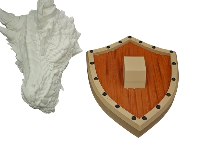 Puede incluir: Una escultura de cabeza de drag&oacute;n blanca con una superficie texturizada detallada. La escultura est&aacute; montada en un escudo de madera con un patr&oacute;n de veta de madera marr&oacute;n y naranja. El escudo tiene un borde beige y detalles met&aacute;licos negros.