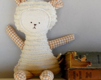 May include: A white plush lamb toy with brown gingham fabric accents. The lamb is sitting on a shelf with a stack of old books.