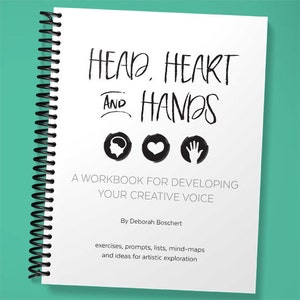 Op de afbeelding: Een wit werkboek met een zwarte spiraalbinding. De omslag heeft de tekst "HEAD, HEART AND HANDS" in zwarte handgeschreven letters. Onder de tekst staan drie zwarte pictogrammen: een brein, een hart en een hand. De tekst "A WORKBOOK FOR DEVELOPING YOUR CREATIVE VOICE" staat onder de pictogrammen. De naam van de auteur, "By Deborah Boschert", staat onder de tekst. De tekst "exercises, prompts, lists, mind-maps and ideas for artistic exploration" staat onderaan de omslag.