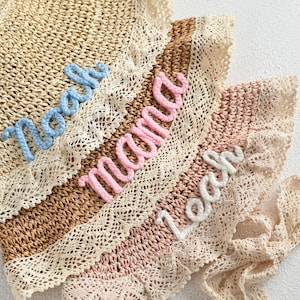 Può includere: Tre cappelli di paglia con bordo in pizzo e parole ricamate. Il cappello superiore ha "Noelle" ricamato in blu, il cappello intermedio ha "mama" ricamato in rosa e il cappello inferiore ha "beach" ricamato in bianco.