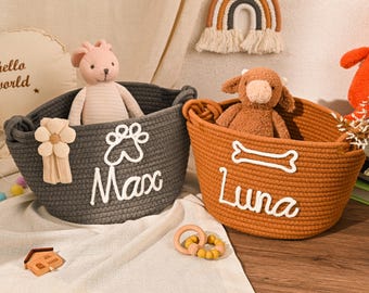 Könnte beinhalten: Zwei ovale Aufbewahrungskörbe aus Seil in Dunkelgrau und Orange. Der graue Korb zeigt eine weiße Pfote und den Namen Max, während der orangefarbene Korb einen weißen Knochen und den Namen Luna aufweist. Beide Körbe haben integrierte Griffe.