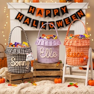 May include: Three fabric buckets with handles, featuring gingham patterns in black, lavender, and orange. Each bucket has a ruffled top edge and a name embroidered in white or orange script: Sonny, Elle, and Luca. The buckets are filled with candy.