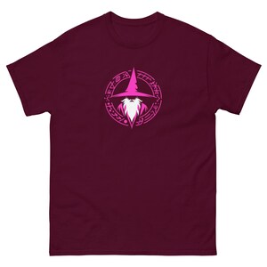 May include: Burgundy t-shirt featuring a pink wizard graphic within a circular design. The wizard has a long white beard and a pointed hat. The graphic is centered on the front of the shirt.