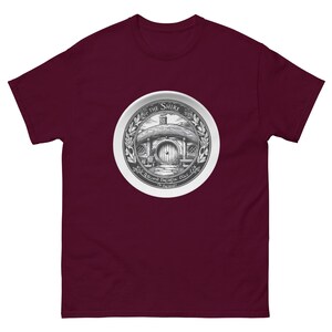 May include: Burgundy t-shirt featuring a circular graphic of a hobbit hole with the text "The Shire" and "Second Breakfast Place". The graphic is in black and white, surrounded by a laurel wreath.
