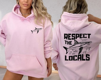 May include: Pink hoodie with a shark graphic on the front and the text "Respect the Locals" with a shark graphic on the back.