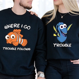May include: Matching navy blue sweatshirts featuring cartoon fish designs. One sweatshirt has an orange fish with the text "WHERE I GO TROUBLE FOLLOWS." The other has a blue fish with the text "TROUBLE."