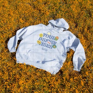 May include: A light gray hoodie with a front pocket and a hood, featuring the text "Your Design Here" in a colorful design. The hoodie is set against a backdrop of vibrant orange flowers.