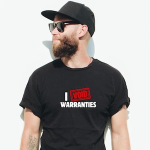 May include: A man wearing a black t-shirt with the text "I VOID WARRANTIES" in white letters and a red stamp. He is wearing a black baseball cap and sunglasses.