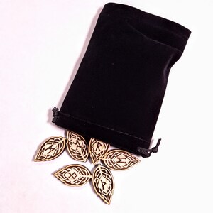 May include: A black velvet pouch with a drawstring closure, spilling out wooden leaf-shaped tiles with intricate designs.