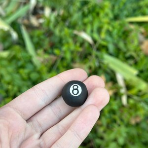 Könnte beinhalten: Eine schwarze Billardkugel mit der Nummer 8 in weiß.