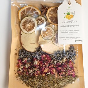 May include: A clear plastic bag filled with dried fruit slices, star anise, and a mix of dried herbs and flower petals. The bag has a tag that reads "Spring Fresh SIMMER POTPOURRI". The ingredients include apples, lemon, lime, lavender, rose petals, mint, and star anise.