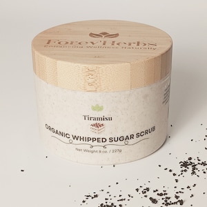 May include: A white jar with a bamboo lid labeled "Forev'Herbs Enhancing Wellness Naturally". The jar contains a white sugar scrub with the text "Tiramisu Organic Whipped Sugar Scrub Net Weight 8 oz. / 227g".