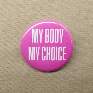 May include: Pink button badge with the text "My Body My Choice" in white lettering.