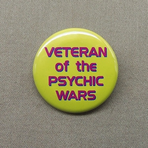 May include: A yellow button with the text "Veteran of the Psychic Wars" in pink and blue letters.