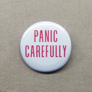 May include: White button with the text "PANIC CAREFULLY" in pink lettering.