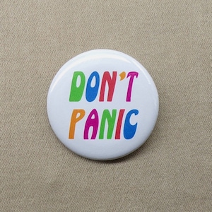 May include: White button with the text "DON'T PANIC" in rainbow colors.