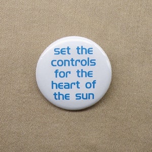 May include: White button with blue text that reads "Set the controls for the heart of the sun".
