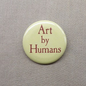 May include: A yellow button with the text "Art by Humans" in brown lettering.