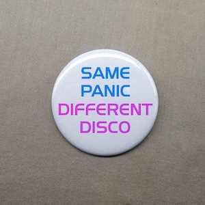 May include: White round button with the text "SAME PANIC DIFFERENT DISCO" in blue and pink lettering.