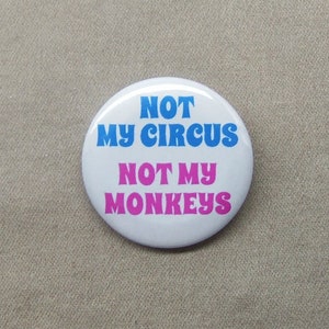 May include: White button with the text "NOT MY CIRCUS NOT MY MONKEYS" in blue and pink lettering.