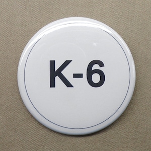May include: White round sign with black text that reads "K-6".