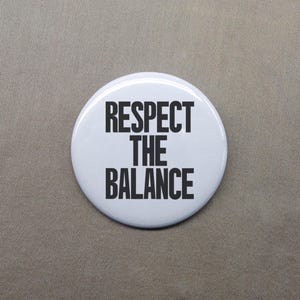 May include: White round button with black text that reads "Respect the Balance".