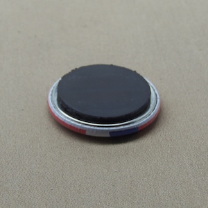 May include: A round magnet with a black magnetic backing and a white, red, and blue design. The magnet is approximately 2 inches in diameter.