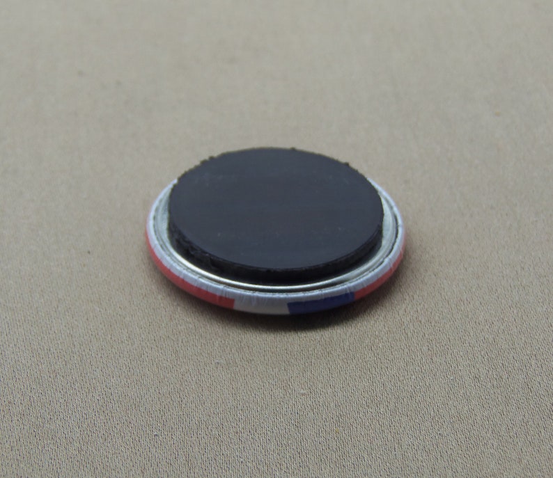 May include: A round magnet with a black magnetic backing and a white, red, and blue design. The magnet is approximately 2 inches in diameter.