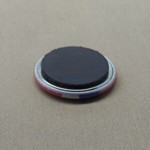 May include: A round magnet with a black magnetic backing and a white, red, and blue design. The magnet is approximately 2 inches in diameter.