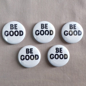May include: Five white round buttons with the words "BE GOOD" in bold black letters. The buttons are arranged in a slightly offset pattern against a neutral background.