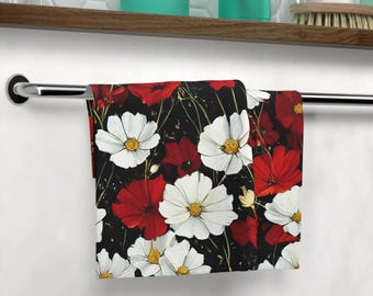 May include: A folded towel with a floral pattern of red and white flowers against a black background. The towel is hanging on a chrome towel bar in a bathroom setting. The flowers have yellow centers.