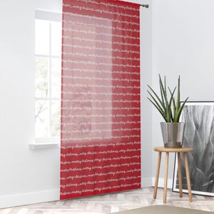 May include: Red sheer curtain with the words "merry christmas" in a repeating pattern. The curtain hangs in front of a window, with a plant and a small wooden table to the right.