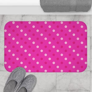 May include: A pink bath mat with a white polka dot pattern.