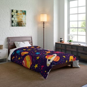 May include: A dark purple comforter with a colorful space-themed design featuring planets, stars, and other celestial elements. The comforter is on a wooden bed frame in a well-lit room with a large window.