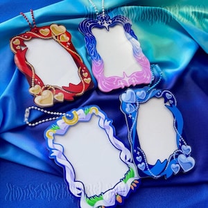 May include: Four decorative acrylic frames in red, blue, and purple hues, each with a unique design. The frames feature heart, ribbon, and star motifs, with a blank center for personalization. Each frame has a chain for hanging.
