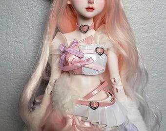 May include: A doll with long, pale pink hair and a white fur hat with pink ears. The doll is dressed in a pink and white outfit with heart-shaped details and a matching choker. The doll's makeup includes pink blush and lipstick.