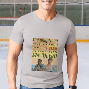 May include: A grey t-shirt with a vintage-style graphic that reads "The only thing better than a glass of beer is tea with Ms McGill". The graphic features a man and a woman in a retro setting.