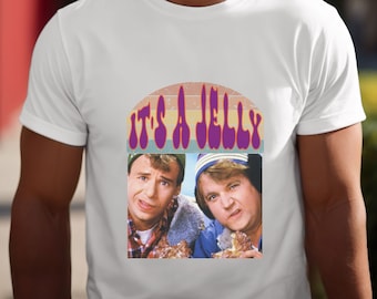 May include: White t-shirt featuring a retro design with the text "IT'S A JELLY" in purple, above a picture of two men. The design has a vintage, colorful aesthetic, with a rainbow-colored arch behind the text.