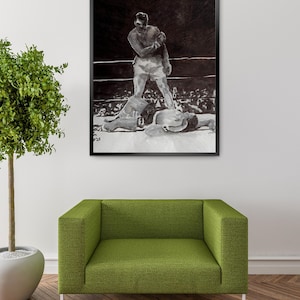 Puede incluir: Impresión en blanco y negro enmarcada de un combate de boxeo. La obra de arte representa a dos boxeadores en un ring, uno de pie sobre el otro. La impresión se muestra encima de un sofá verde y junto a una planta en maceta.